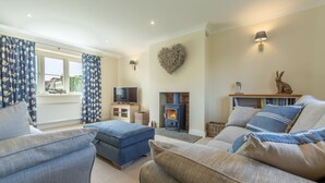 A cozy living room with a fireplace, comfortable sofas, a television, and a heart-shaped wall decoration. - Stone Croft, Barney, Norfolk (Barney)