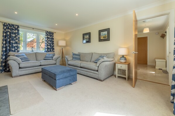 A living room with two sofas, a blue ottoman, and a lamp on a side table.