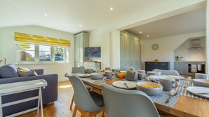 A modern kitchen with a dining area, featuring a TV, cabinets, and a clock on the wall. - Stone Croft, Barney, Norfolk (Barney)