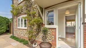A house with a stone exterior, a small garden, and a visible kitchen area through the open door. - Stone Croft, Barney, Norfolk (Barney)