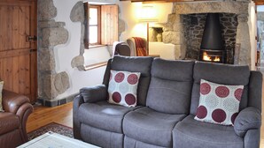 Un salon chaleureux avec une cheminée en pierre, des poutres apparentes et un canapé en cuir agrémenté de coussins à motifs.
