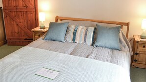 Un lit bien fait, avec un oreiller à rayures, une tête de lit en bois et deux tableaux encadrés accrochés au mur.