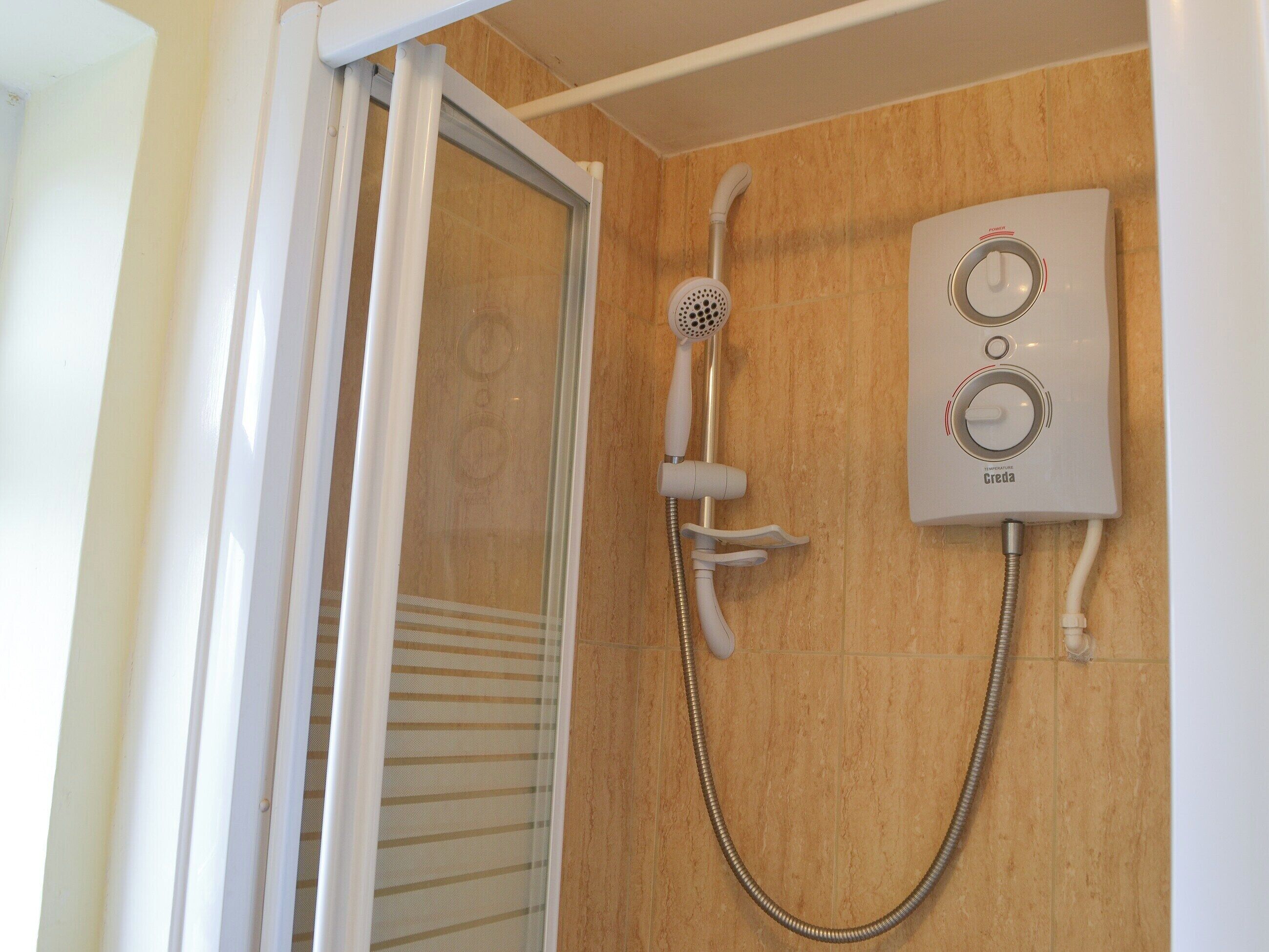 Une douche équipée d’un pommeau de douche à main et d’un panneau de commande fixé au mur.
