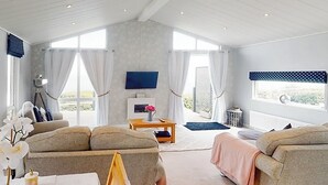 En rummelig stue med sofasæt, TV og udsigt til det fri.