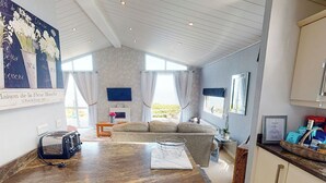 Et moderne køkken med en central ø, et spiseområde med en sofa, og udsigt til det fri.