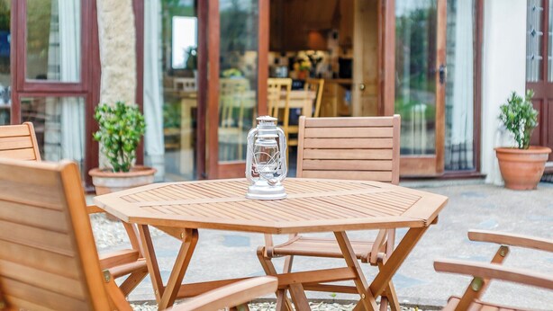 Un juego de mesa de madera con sillas dispuesto frente a un edificio con tejado de paja.