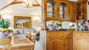 Una cocina de madera con una mesa de comedor, sillas y una araña. Hay un espejo en la pared y una ventana con cortinas.