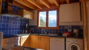 Een keuken met houten kastjes, een raam met uitzicht op de bergen, een vaatwasser en een wasmachine.