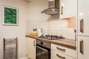 A modern kitchen with white cabinets, a stainless steel range hood, a built-in oven, and a tiled backsplash.