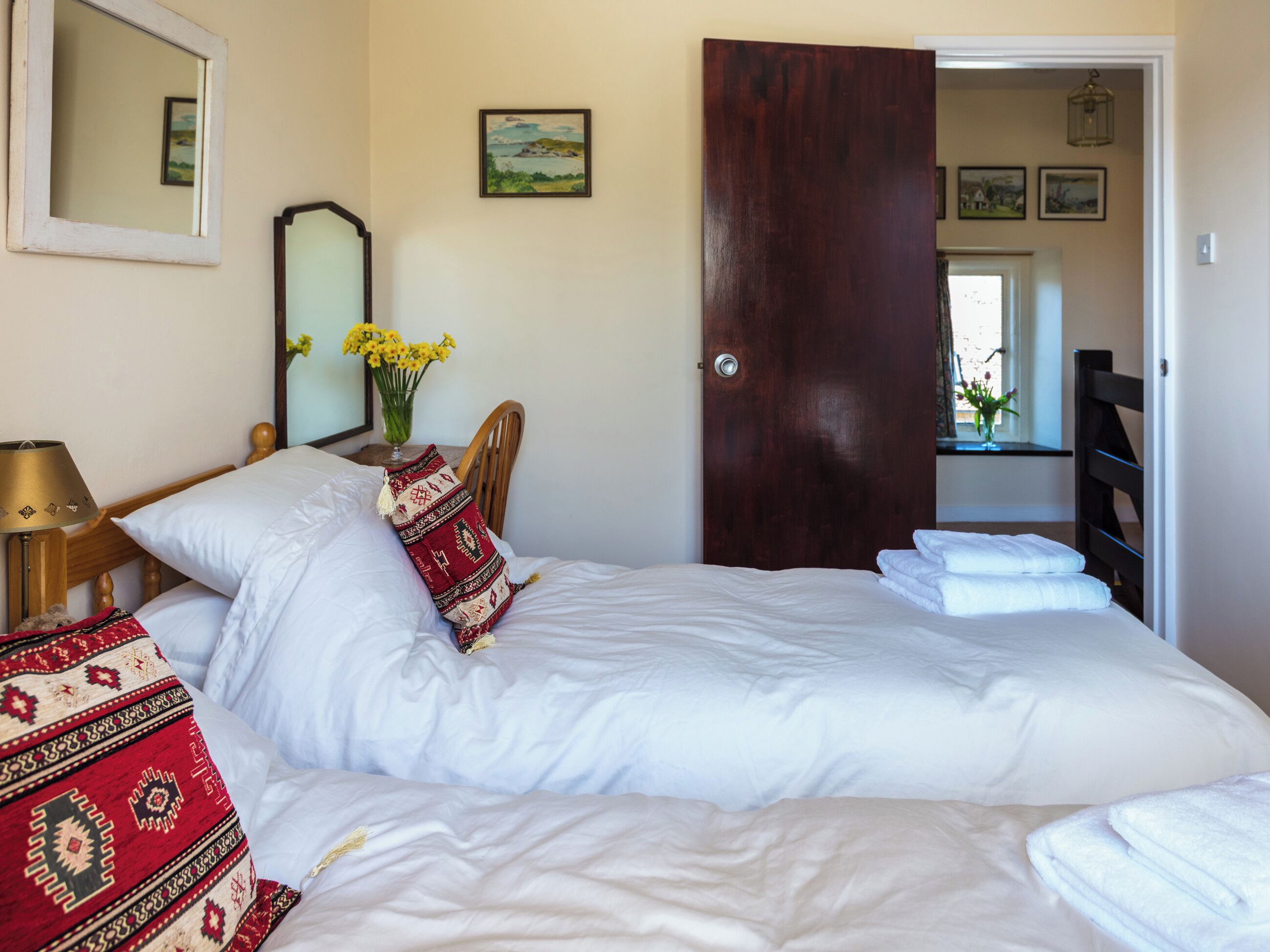 Un dormitorio con una cama grande, un cabecero de madera, una mesita de noche con una lámpara, un espejo y un jarrón con flores.