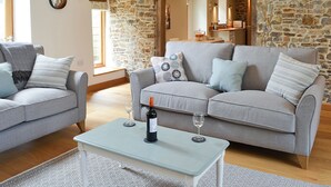 Una sala de estar con un sofá gris, una mesa de centro con una botella y una copa de vino, y paredes de piedra.