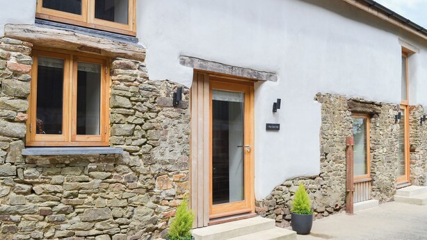 Un edificio de piedra con ventanas de madera y una puerta, una pequeña planta en maceta, y un letrero que dice 'The Old Mill'.
