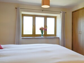 A bedroom with a large bed, a window with curtains, a vase with flowers, and a wooden wardrobe. - Upper Close - UK10873 (Prestrigne)