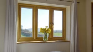 A bedroom with a large window, curtains, and a vase with flowers. - Upper Close - UK10873 (Prestrigne)