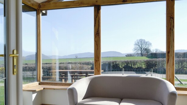 A room with a sofa, large windows, and a view of a countryside landscape. - Upper Close - UK10873 (Prestrigne)
