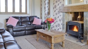 A living room with a leather sofa, a wooden coffee table, a fireplace, and patterned wallpaper. - Upper Close - UK10873 (Prestrigne)