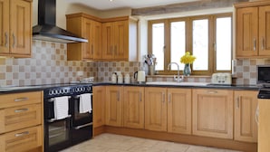 A kitchen with wooden cabinets, a stove, a sink, and a window with natural light. - Upper Close - UK10873 (Prestrigne)