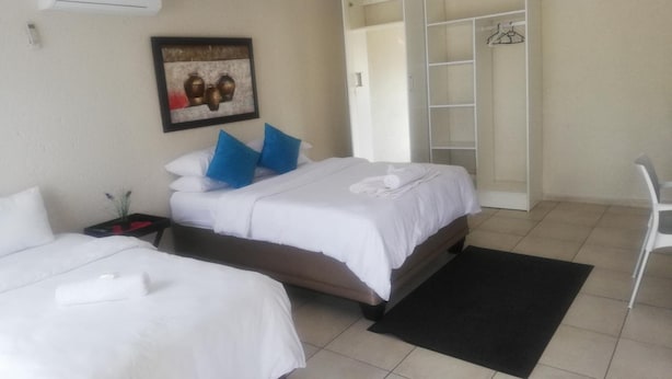 A hotel room with two beds, a black rug, a white chair, and a wardrobe with a mirror. - BTV Guesthouse (Mbombela)