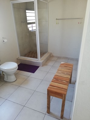 A bathroom with a toilet, shower, and wooden bench. - BTV Guesthouse (Mbombela)