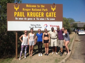 A group of people standing in front of a sign welcoming visitors to Kruger National Park at the Paul Kruger Gate. - BTV Guesthouse (Mbombela)