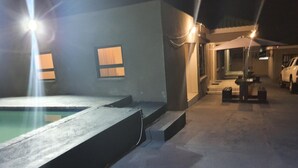 A swimming pool area with a concrete deck, a small outdoor seating area, and a covered patio. - BTV Guesthouse (Mbombela)
