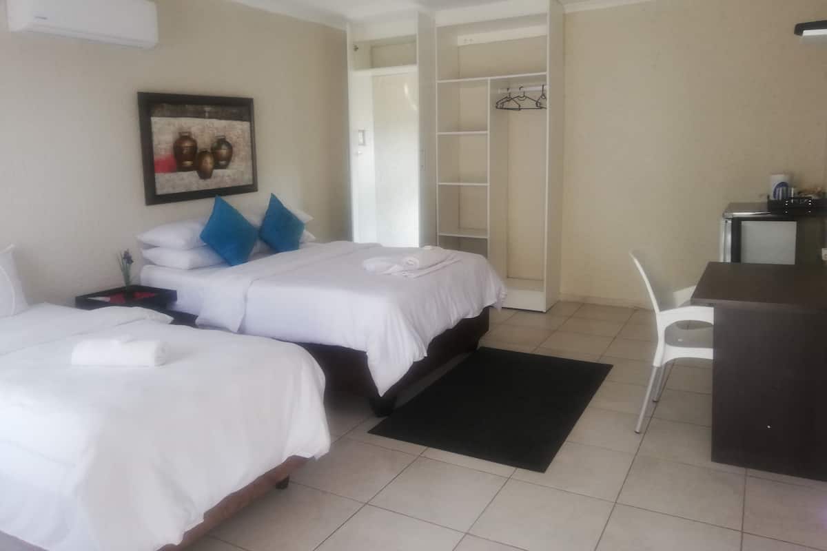 A hotel room with two beds, a desk, a chair, a wardrobe, and a framed picture on the wall.