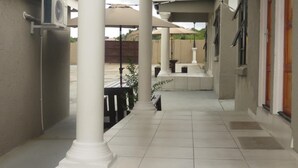 A covered outdoor area with white columns, a tiled floor, and a view of a building in the background. - BTV Guesthouse (Mbombela)
