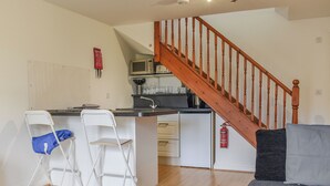 Ein kompakter Wohnraum mit einer Küche, einer Essecke mit zwei Stühlen, einem Sofa und einer Holztreppe.