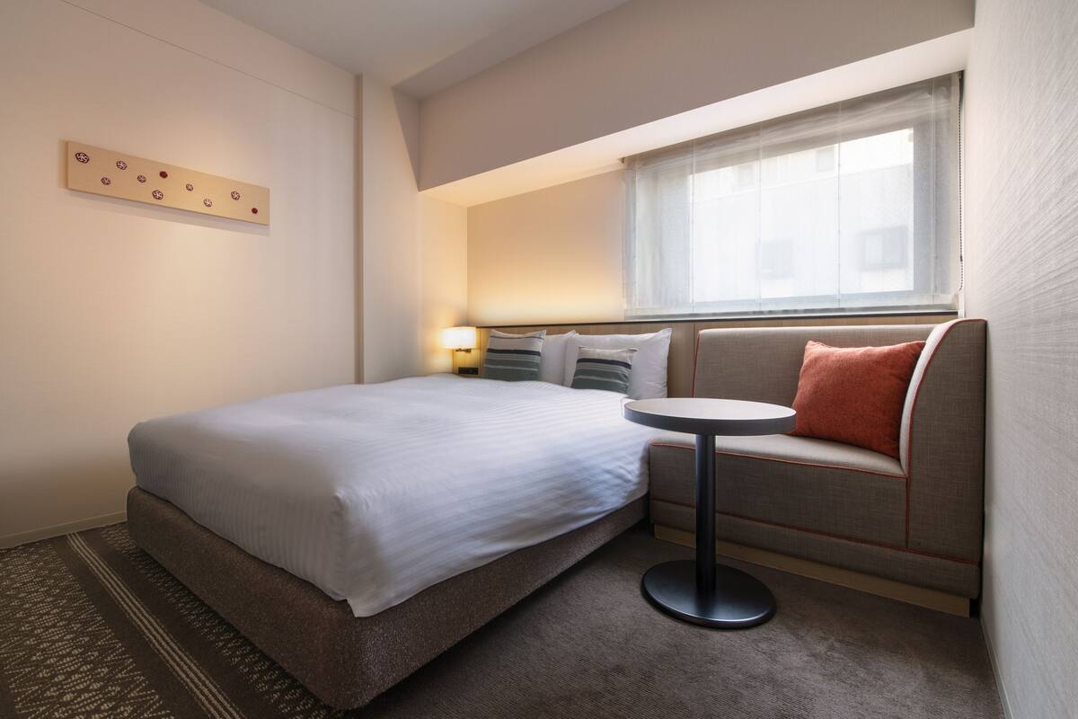 Une chambre d’hôtel avec un lit, un canapé, une petite table et un luminaire fixé au mur.