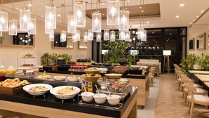 Un área de bufé con diversas opciones de comida, un espacio de comedor con mesas y sillas, y lámparas colgantes.