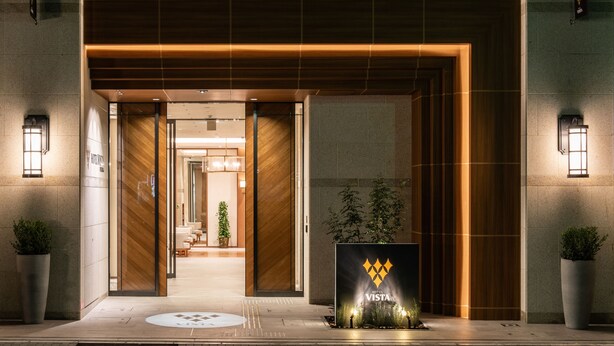 Una entrada de hotel con diseño moderno, que presenta una puerta principal grande, una zona de recepción y un cartel con el nombre del hotel.
