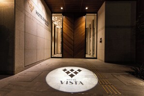 A hotel entrance with a modern design, featuring a prominent logo on the floor and a wooden panel wall. - Hotel Vista Fukuoka Nakasu-Kawabata (Fukuoka)