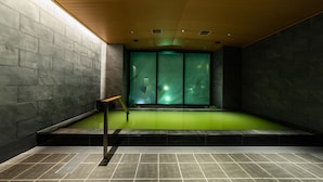 Un área de piscina interior moderna con un banco y vistas a una habitación iluminada en verde a través de un muro de cristal.