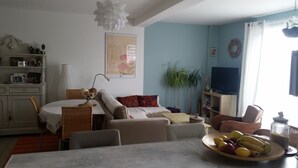 A living room with a dining table, chairs, a sofa, a TV, and a plant. - QUIET AND SERENITY - SEASIDE (VAUX SUR MER)