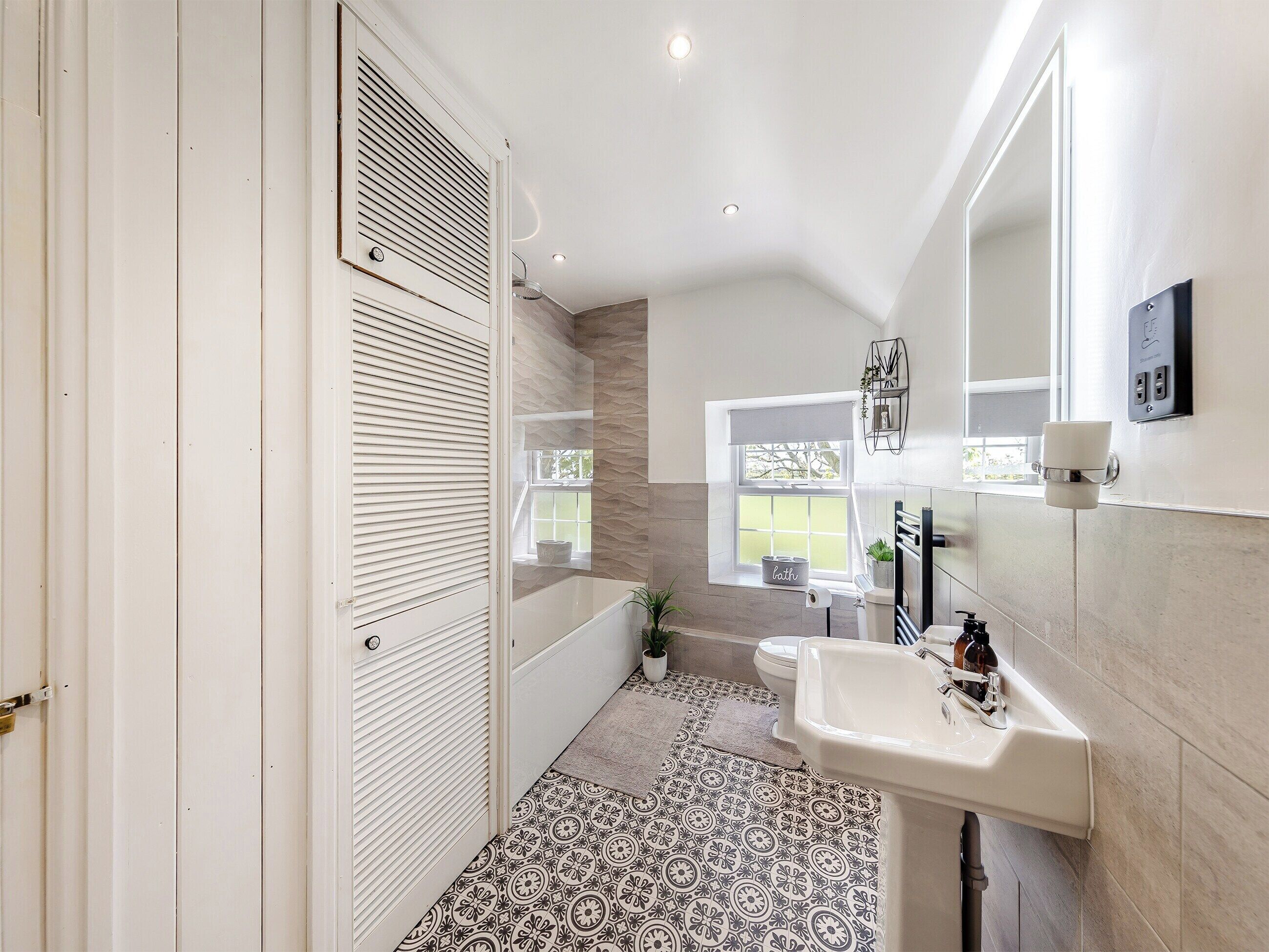 A modern bathroom with a bathtub, toilet, and sink. There is a window providing natural light and a view of the outdoors.