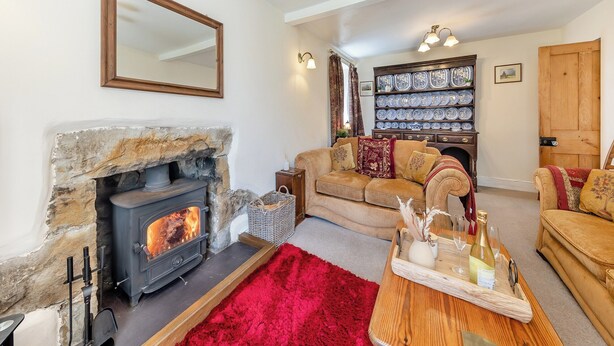 A cozy living room with a stone fireplace, a sofa, a wooden coffee table with a tray, and a wall-mounted plate rack. - 3 bedroom accommodation in Tudweiliog, near Pwllheli (Tudweiliog, near Pwllheli)