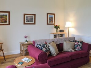 Ett mysigt vardagsrum med en röd soffa, ett litet träbord och en bokhylla.