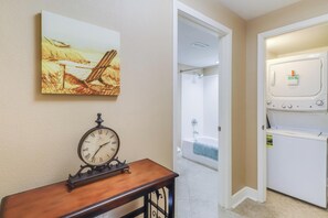 A hallway with a wooden bench, a wall clock, a painting, a bathtub, and a refrigerator.