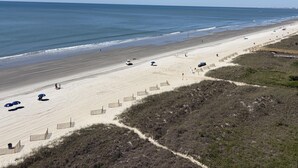 Een strand met een heldere lucht, zandstrand en een houten boardwalk naar het water.