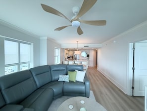 Una sala de estar moderna con un sofá modular, un ventilador de techo y vistas a la cocina.