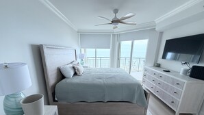 Een slaapkamer met een bed, een plafondventilator, een televisie, een dressoir en uitzicht op de omgeving.