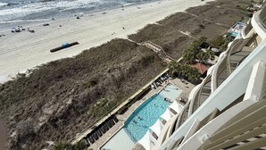 Vistes a la platja des del balcó d'un hotel, piscina i platja amb persones i ombrelles.