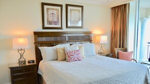 A neatly made bed with a white bedspread and several pillows, flanked by two bedside tables with lamps, a wooden headboard, and two framed pictures on the wall.