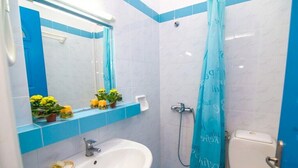 Une salle de bain avec un lavabo blanc, des murs recouverts de carreaux bleus, un rideau de douche et des toilettes.