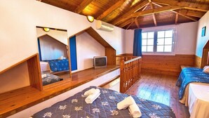 Une chambre confortable située dans les combles, avec des poutres apparentes, un lit en mezzanine, une petite télévision et une fenêtre avec des rideaux.