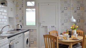 A compact kitchen with a washing machine, a sink, and a dining area with a table set for breakfast.