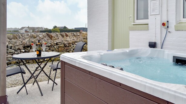 A hot tub with a stone wall and a table with drinks in the background.