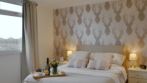 A hotel room with a bed, bedside lamps, a nightstand, a tray with a bottle and glasses, and a window with curtains.