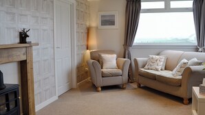 A living room with a fireplace, a sofa, a chair, a lamp, and a window with curtains.