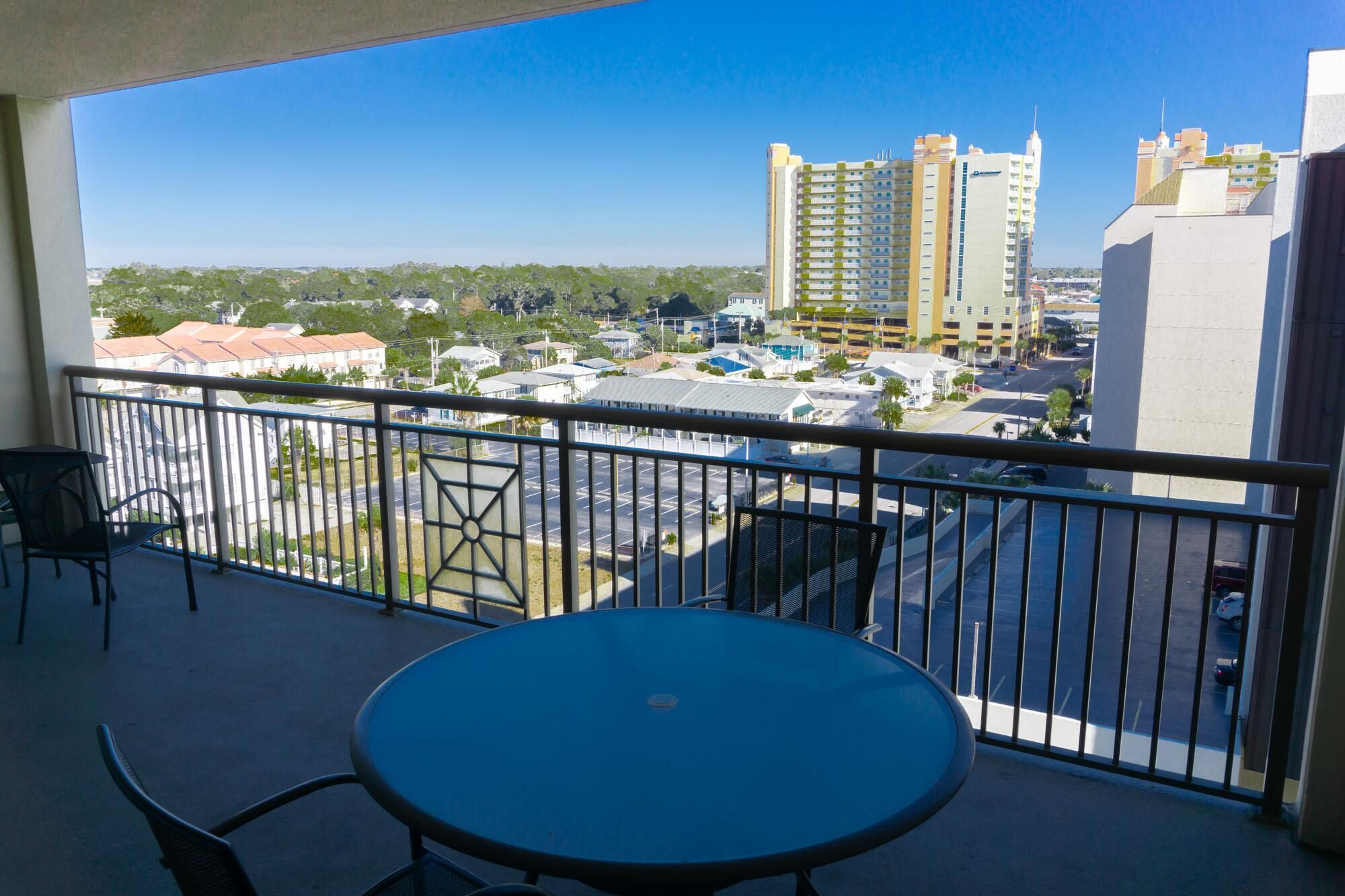 A balcony with a table and chairs, overlooking a parking lot and buildings.